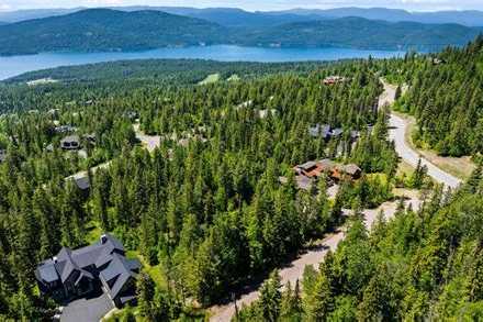 Aerial view over forested Iron Horse homesites and a winding road down to Whitefish Lake, with mountains beyond