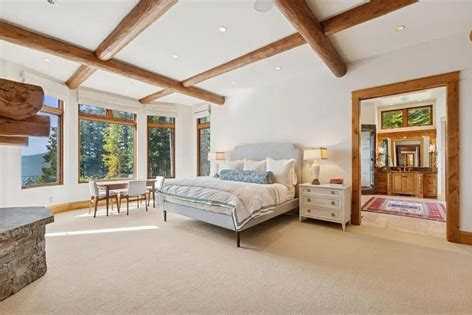 Bright bedroom with log ceiling beams and tall windows looking into evergreens in an Iron Horse home