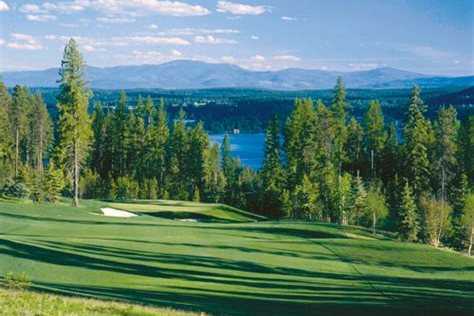Golf fairway lined with evergreens, with Whitefish Lake and distant mountains in view
