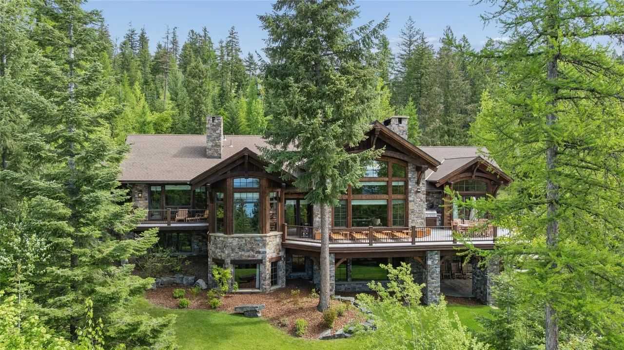 Aerial view of a large timber and stone home with wide decks among tall evergreens in Iron Horse