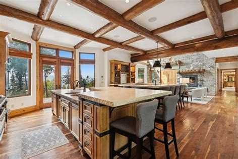 Kitchen with log ceiling beams, a long wood island with bar stools and a stone fireplace in an Iron Horse home