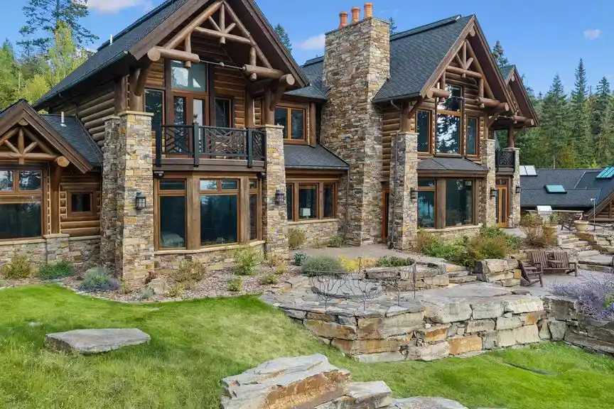 Log and stone home with timber gables, a stone chimney and a terraced stone patio above a lawn in Iron Horse